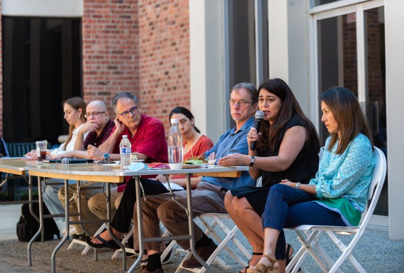 A student and faculty members sit at a long table for a panel discussion.