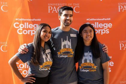 students pose in front of an orange sign reading "California for All College Corps"