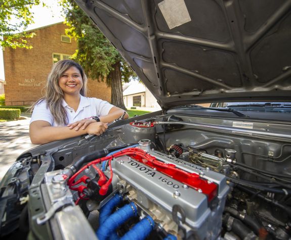 Student sitting behind engine of her custom car