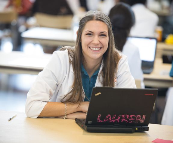 student in white coat in front of laptop