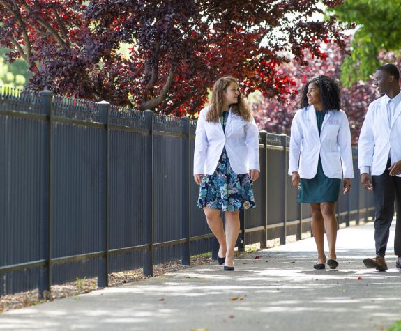 students in white coats walking on sidewalk