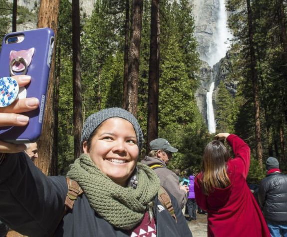 a student takes a selfie at a national park with a waterfall in the background