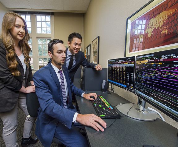 students looking at a computer screen examining stock prices