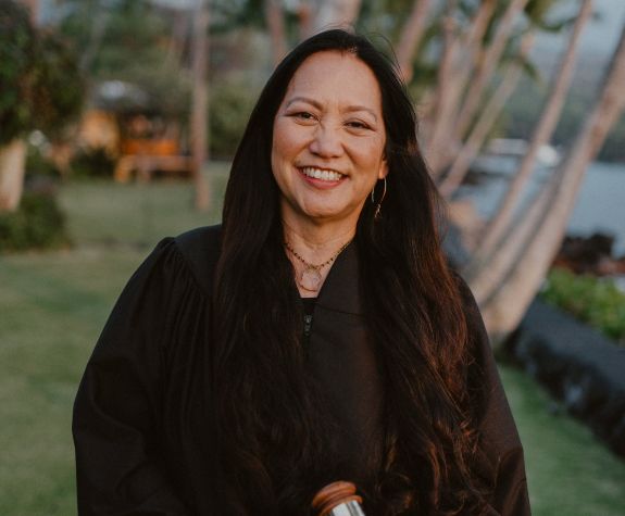 A female judge wearing a robe smiles for a photo outside