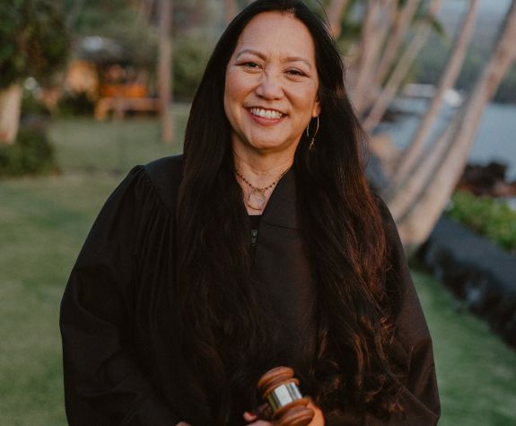 A female judge wearing a robe smiles for a photo outside