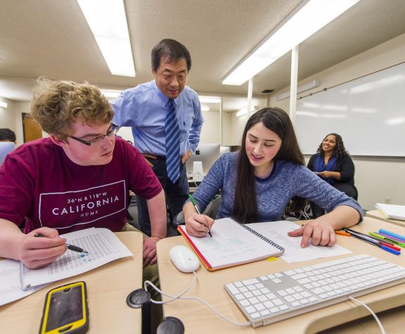 students working at a table with a faculty member helping