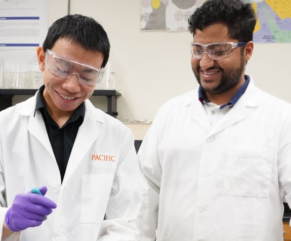 Two PCSP graduate students in a research lab wearing white coats 