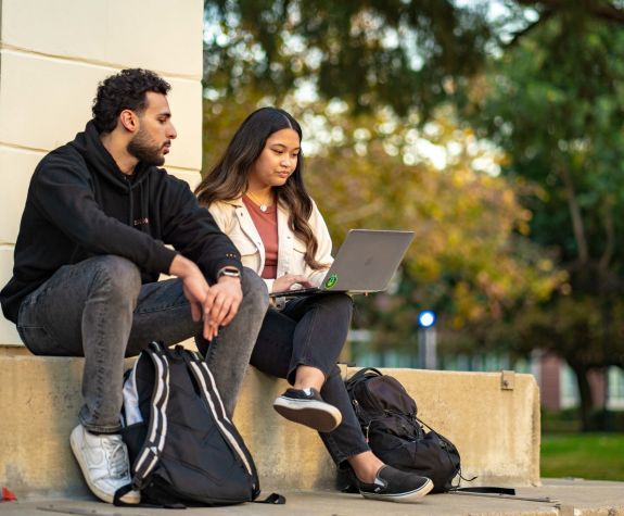 two students sitting outdoors and looking at a laptop screen