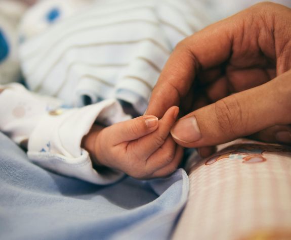 an adult hand holds a baby's hand