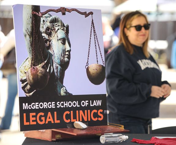 a woman stands in front of a McGeorge Legal Clinics posterboard