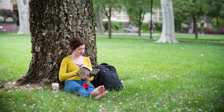 student sitting on lawn with book