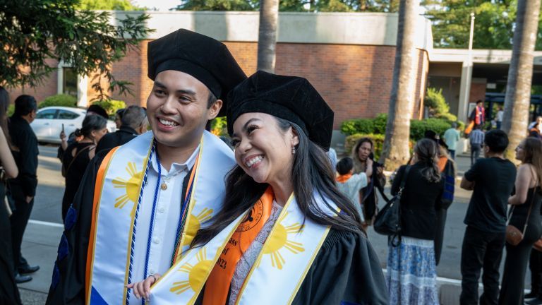 Two students in graduation attire smiling