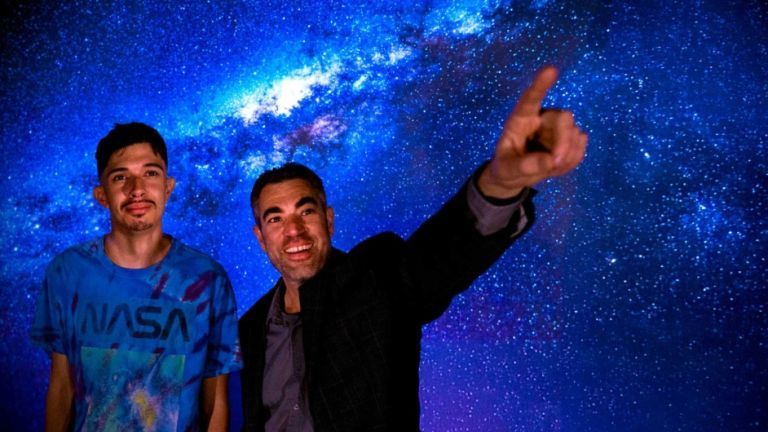 a student and a professor stand together before a galaxy background