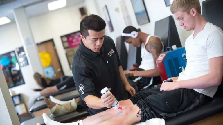 A MSAT student is applying gel to another student's knee in a training simulation