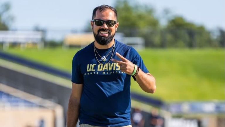 Photo shows Kyle Schank walking on a sports field and smiling. 