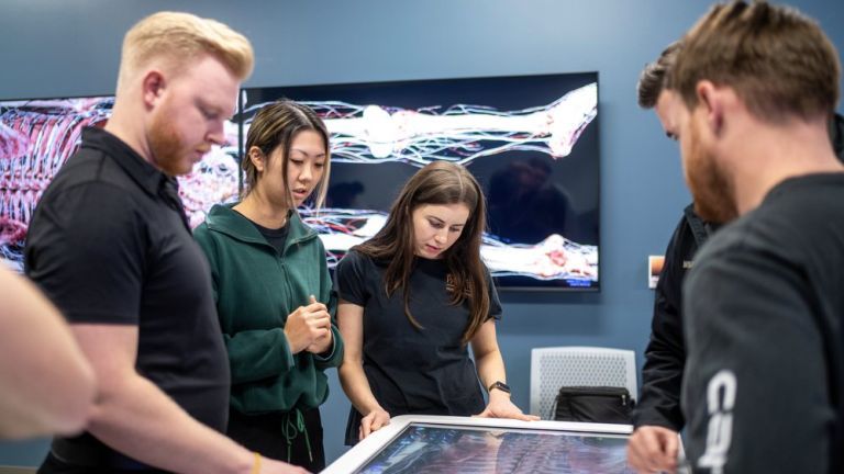 Photos shows several students working on a digital cadaver displayed on an Anatomage table.