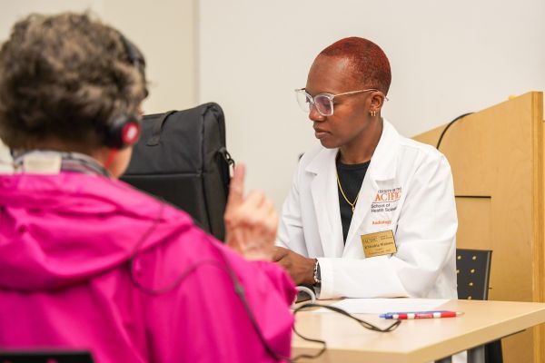 a woman in a white coat sits across a desk from a patient