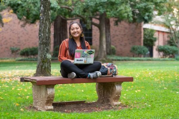 a student sits on a bench with a laptop
