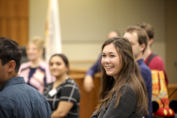 A group of students stands inside, with one woman in the camera focus.