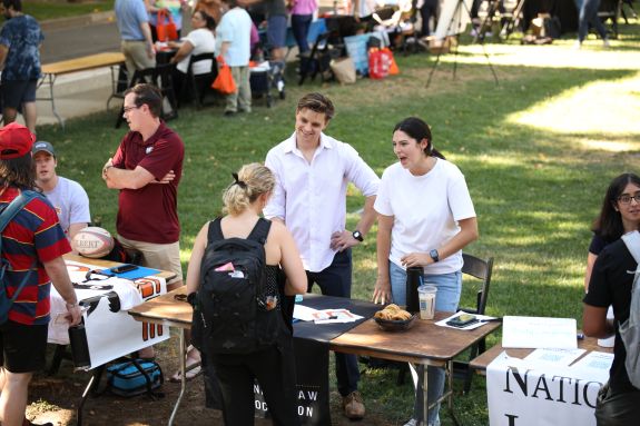 A pair of students offers food to other students at a table.