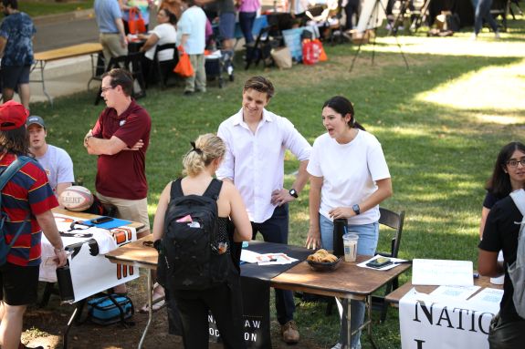 Students stand at a table offering food at a fair.