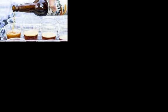 A hand pouring beer into multiple tasting cups