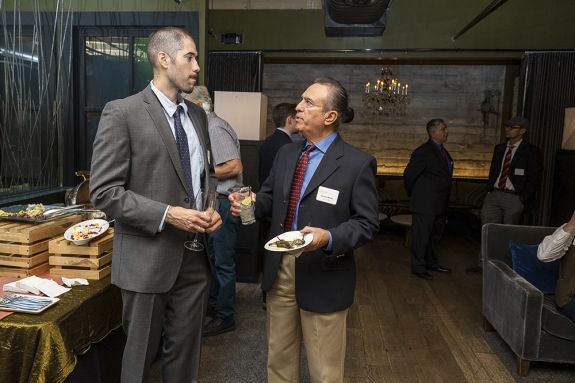 Two men stand in a room talking.