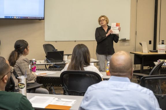 A woman in a black shirts shows the room a book 