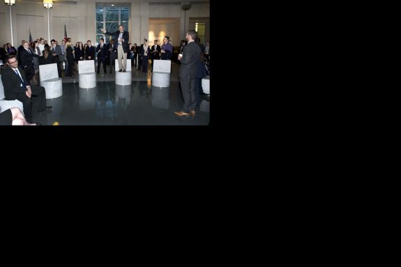 A group of people in suits participate in an event. One man stands on an elevated surface. 