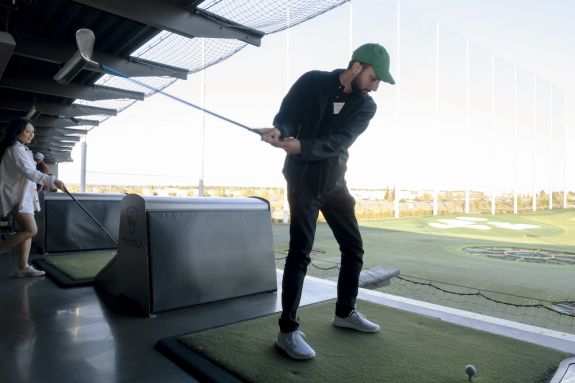 Man in green hat prepares to hit a golf ball