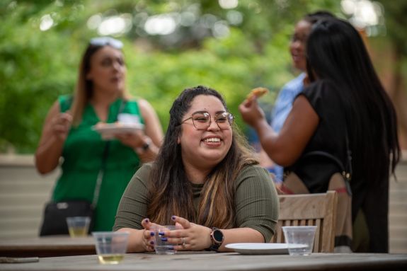 A smiling woman sits at a table outdoors during an event