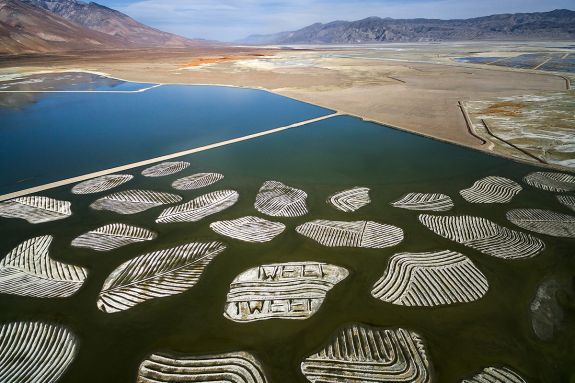 Aerial view of lake bed patterned islands, desert floor, and mountains in the distance.