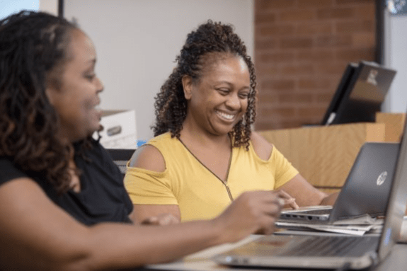 Two women look at laptop computers 