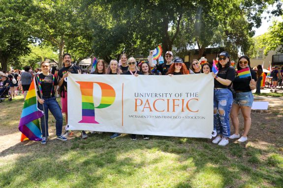 A group of people pose with a pride banner