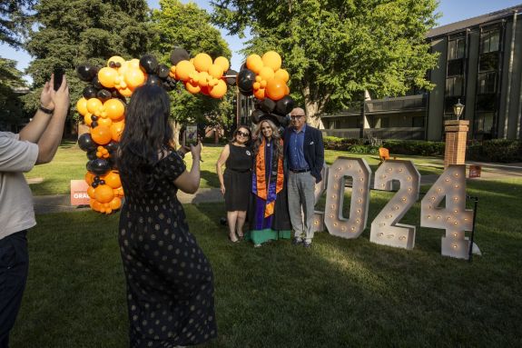 Three individuals poses for a photo in front of a big 2024 sign