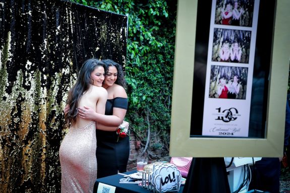 Two women in dresses pose for a photo at a Photo Booth
