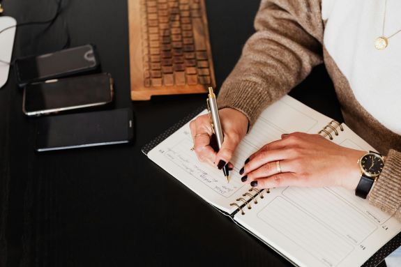 Crop stylish woman writing in notebook