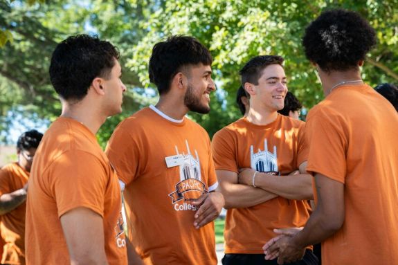 4 college corps fellows outside in orange shirts talking