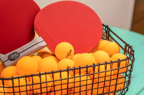 Ping pong paddles in a basket of orange balls.