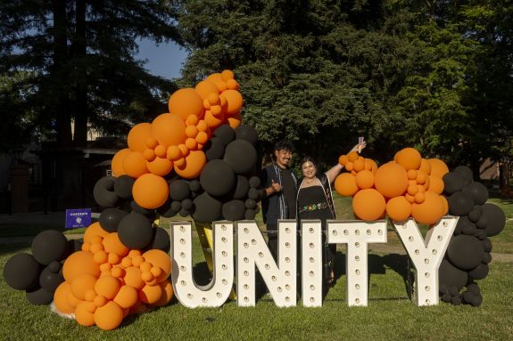 Two people pose by a sign that says "Unity"