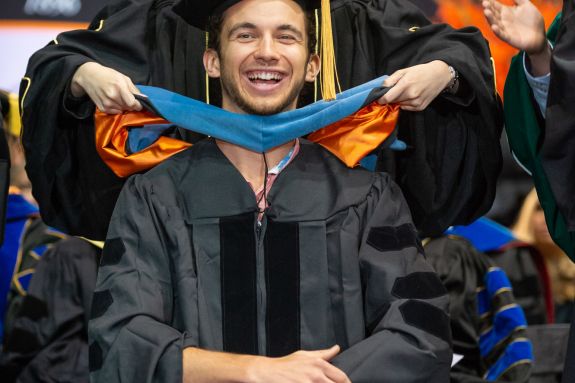 Student getting hooded on stage during TJL School of Pharmacy Ceremony