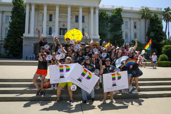 A group of people in black t-shirts smile and pose with rainbow flags