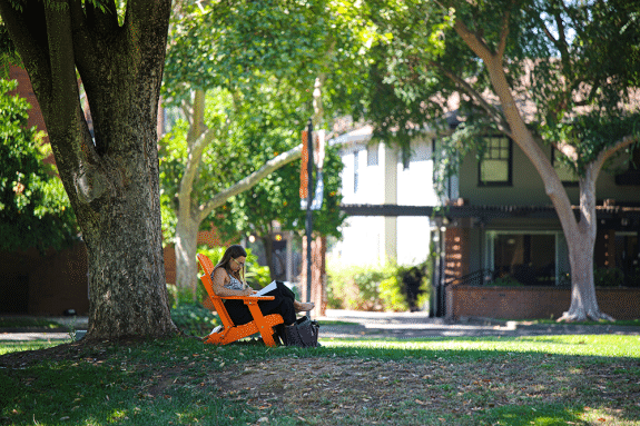 A women sits in a orange chair reading a book. 