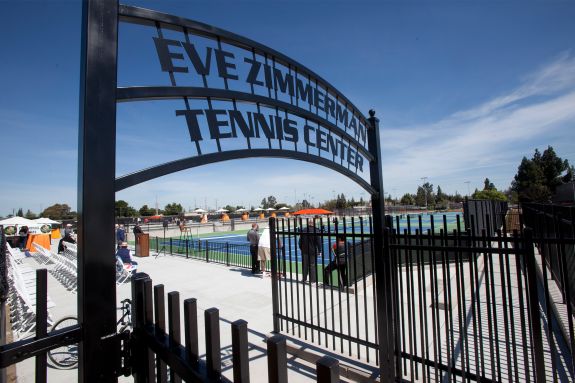 a metal sign reads "Eve Zimmerman Tennis Center" in front of a tennis court