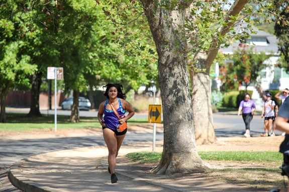 A girl with an orange bag runs in a park. 