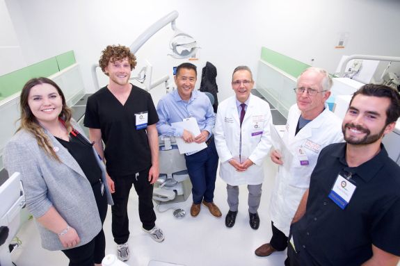 6 people standing in a semi circle facing the camera in the sim lab