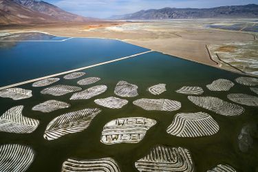 Aerial view of a lake with patterned islands, desert, and mountains in the distance.