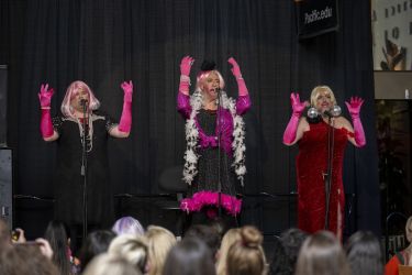 three men in drag clothing perform on stage 