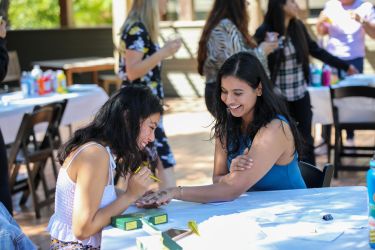 Two students smiling which one student gives the other henna during an event