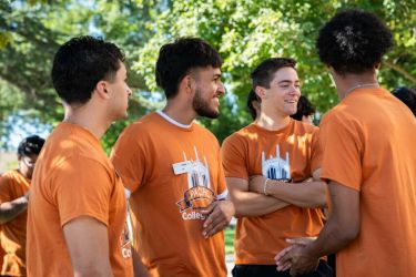 4 college corps fellows outside in orange shirts talking